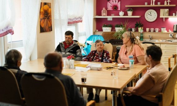 Seniors enjoying a meal in a nursing home dining room with caregivers in Karviná, Czechia.