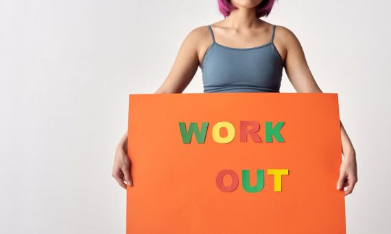 Woman with short hair holding a vibrant 'Work Out' sign on a white background.